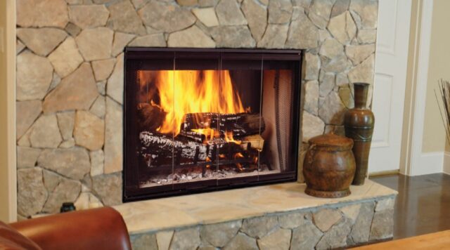 Stone fireplace with a burning fire and glass screen, decorated with ceramic vases beside it.