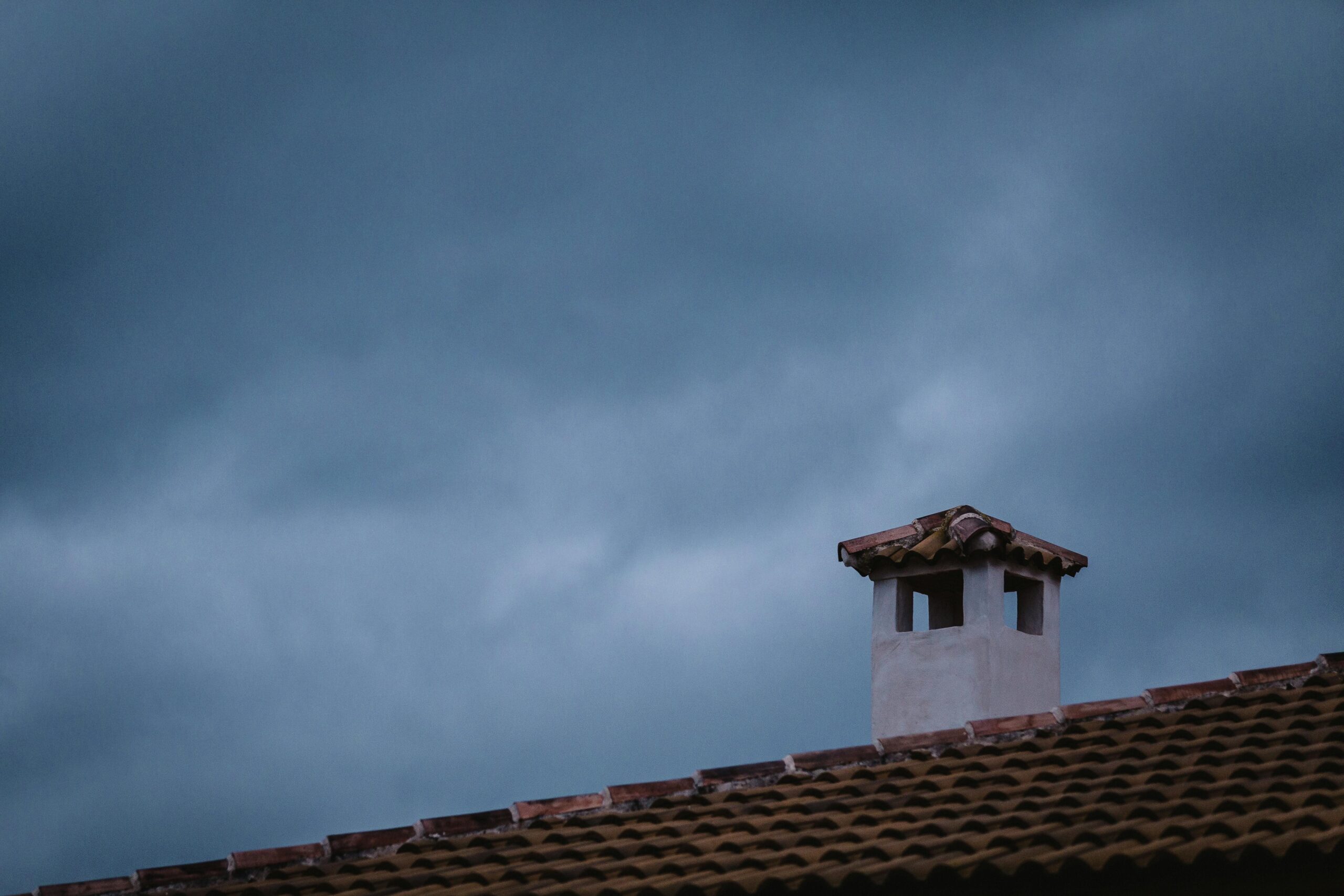 Chimney with protective cap on a tiled roof, preventing rain and debris entry.