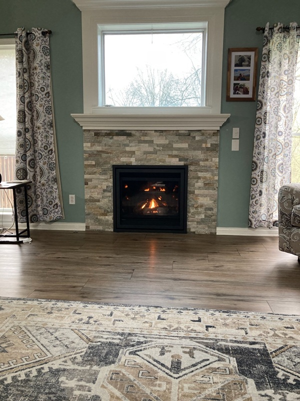 Fireplace with stacked stone surround and white mantel, featuring a lit gas insert.