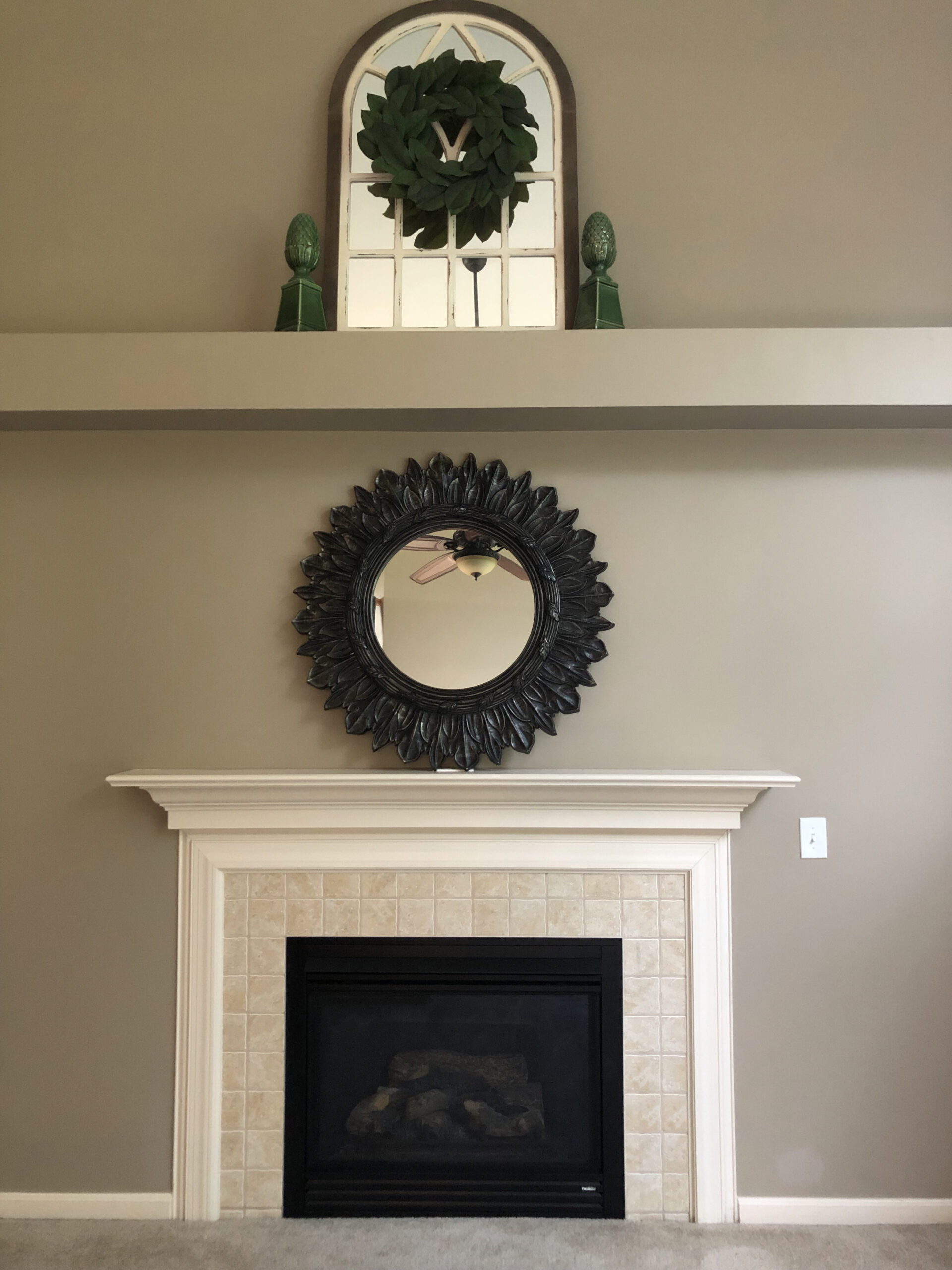 Beige tile fireplace with white mantel, decorated with a round black framed mirror above.