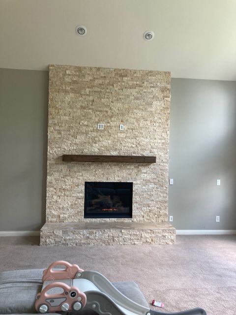 Tall stone fireplace with a simple wooden mantel and black firebox insert.