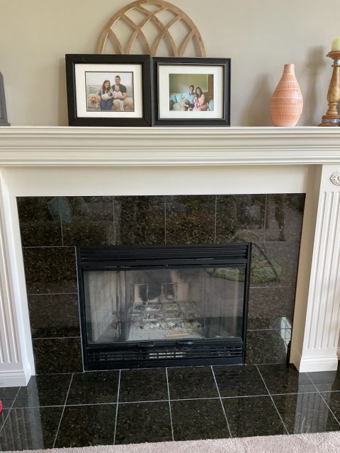 Traditional white mantel fireplace with black granite surround, decorated with framed photos and a vase.