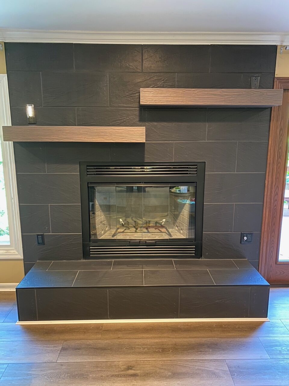 Modernized fireplace with dark tile surround, minimalist wooden shelves, and updated firebox.