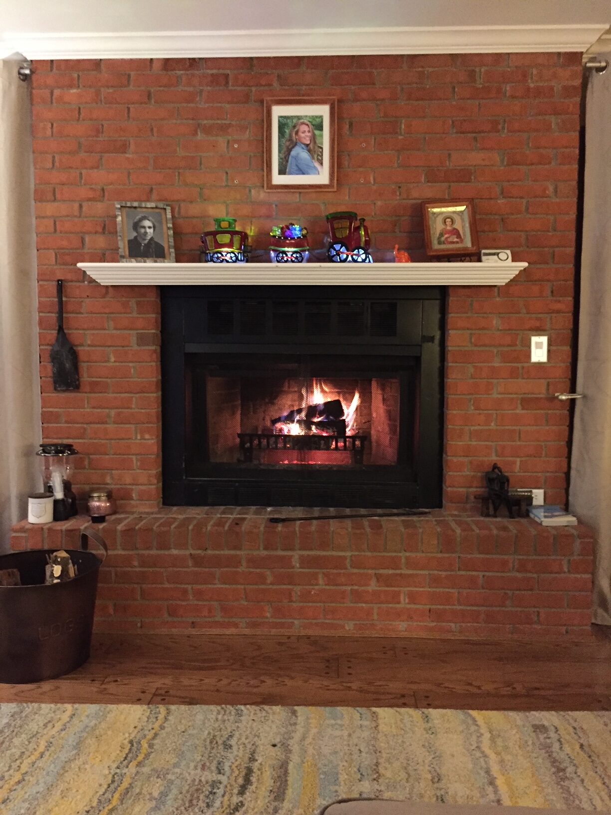 Brick fireplace with white mantel and decorative items, lit with a wood-burning fire.